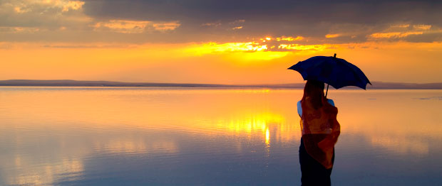 Woman with umbrella watching a sunset over water